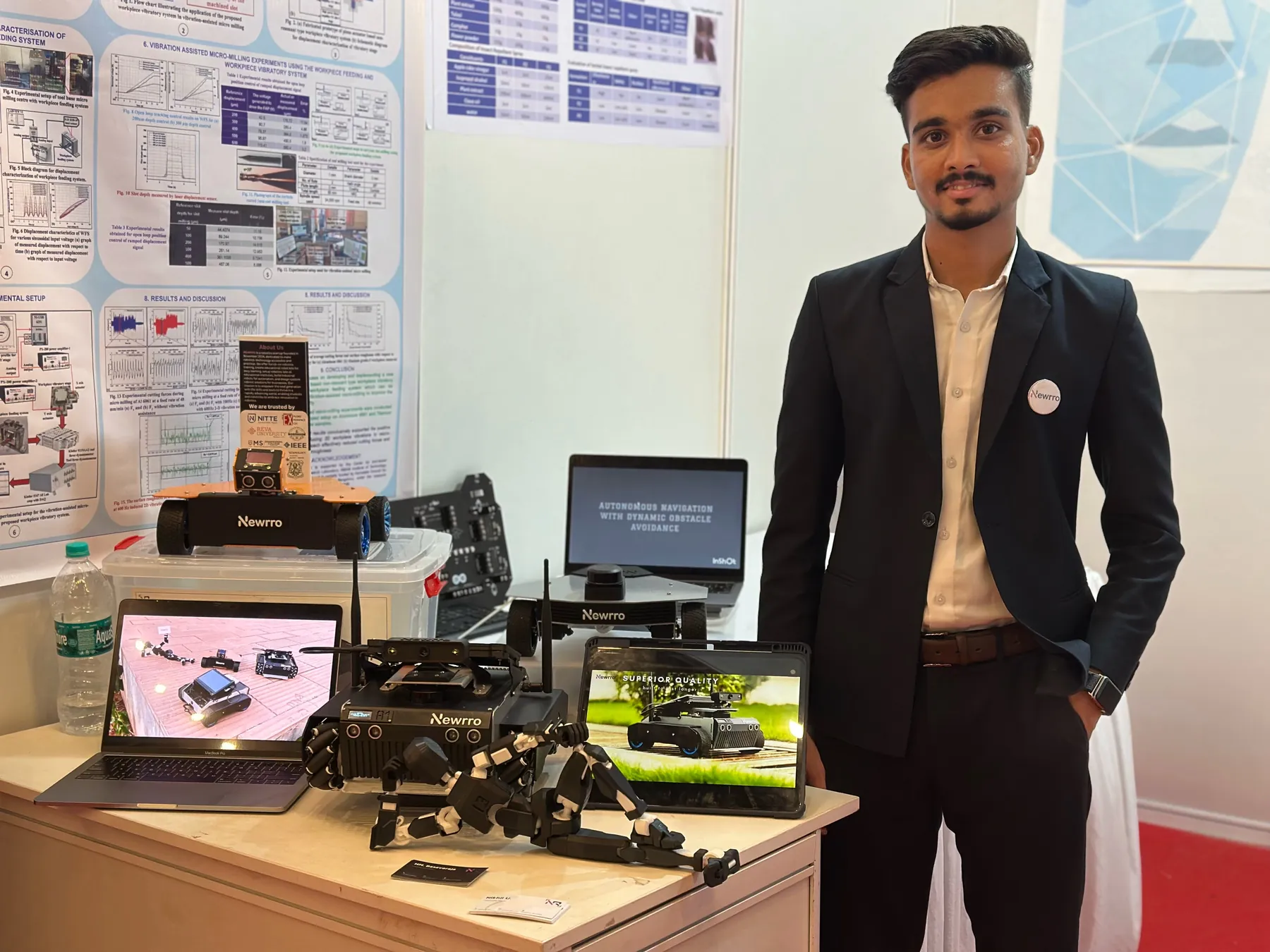 A Newrro team member at the exhibition stand with ARJUNA and a robot arm