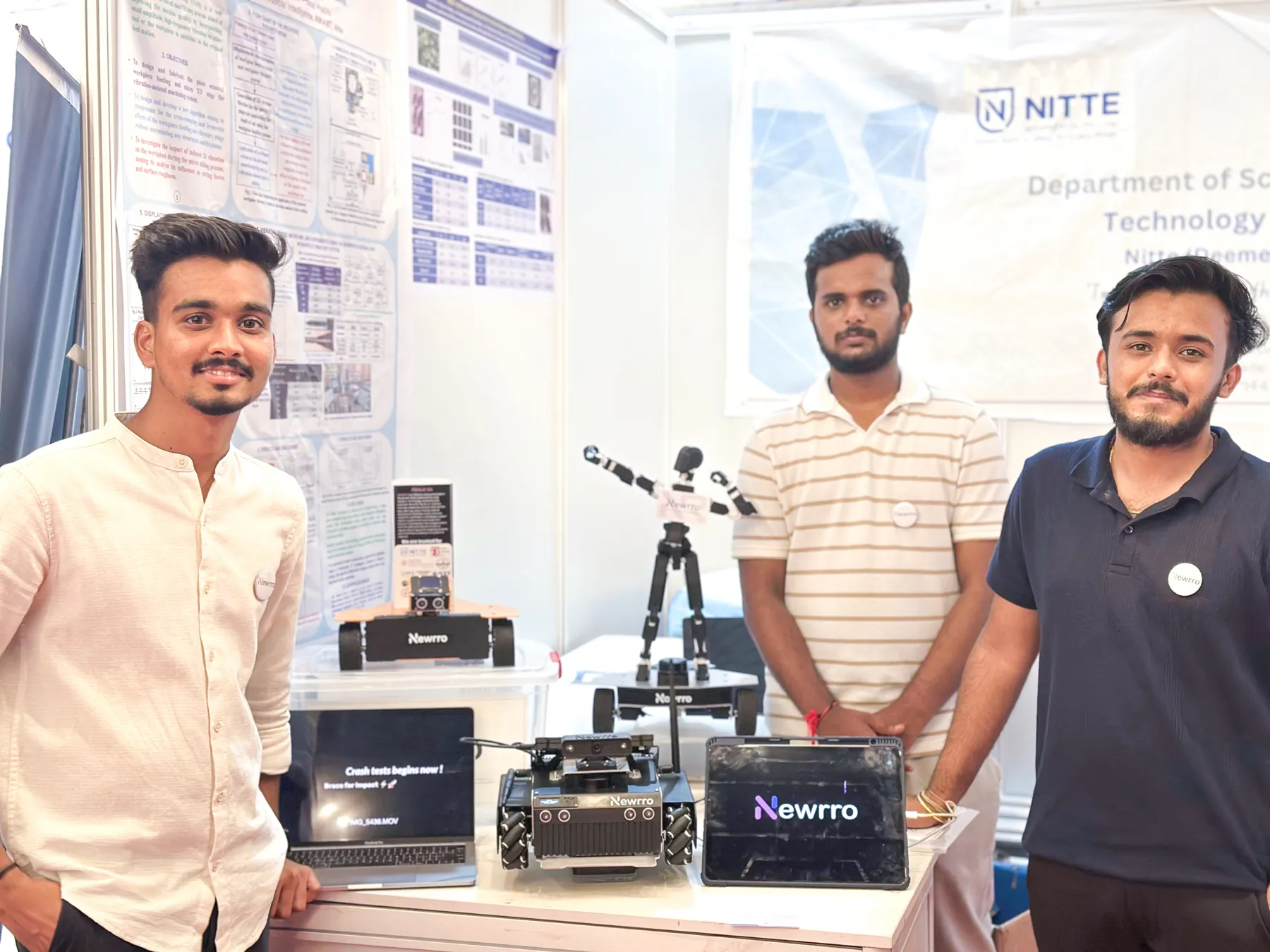 Three members of the Newrro team at their exhibition stand, with ARJUNA and other Newrro robots on the table